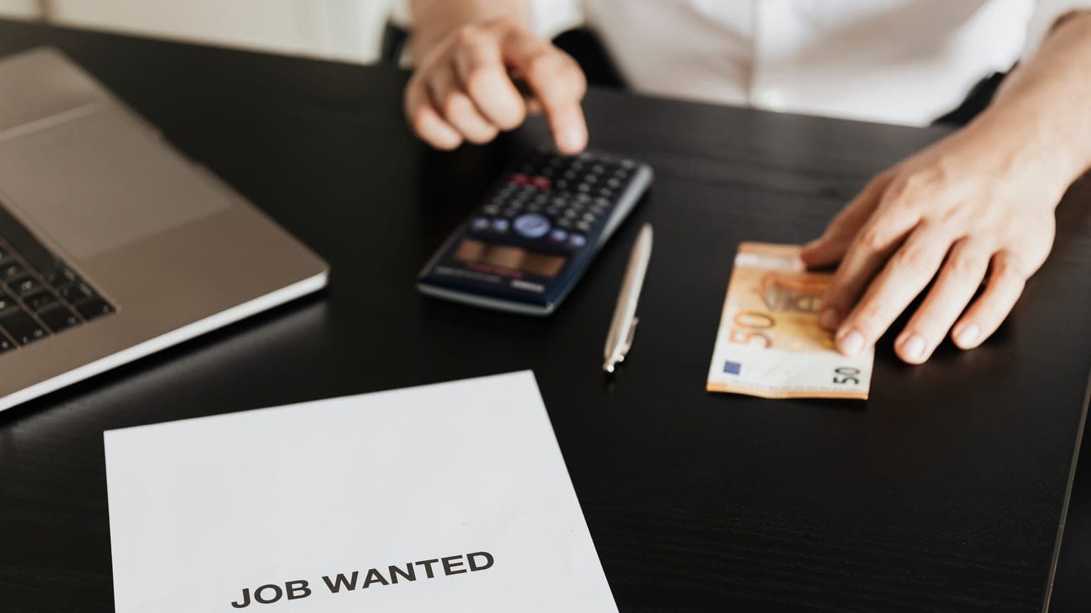 Muž počíta na kalkulačke pri hárku Job Wanted — nárok na odstupné po strate zamestnania